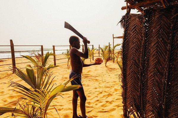 Jeune garçon ouvrant une noix de coco sur la plage ivoirienne